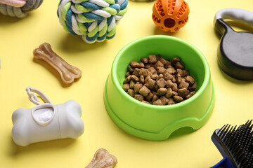 Bowl with pet food and accessories on yellow background, closeup