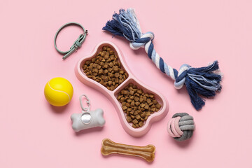 Bowl in shape of bone with dry pet food and accessories on pink background