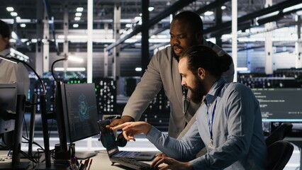 Data center engineers use laptop, collaborating on doing AI software updates. Server room teamworking colleagues doing brainstorming, optimizing infrastructure using artificial intelligence, camera A