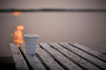 Empty coffee cup on a table at the seashore at dawn with sunrise reflections