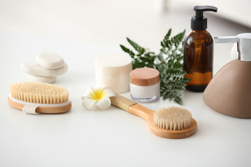 Massage body brushes, flower and jars with cosmetic products on table in room, closeup