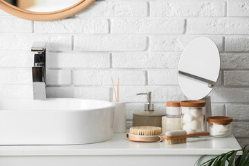 Massage body brushes and jars with cosmetic products on table near sink in bathroom