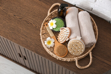 Wicker tray with massage body brushes and towels on chest of drawers in room, closeup