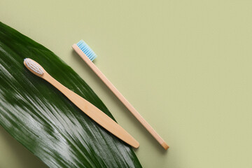Wooden toothbrushes and green leaf on green background, closeup