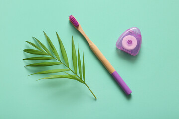 Wooden toothbrush, dental floss and green leaf on turquoise background, closeup