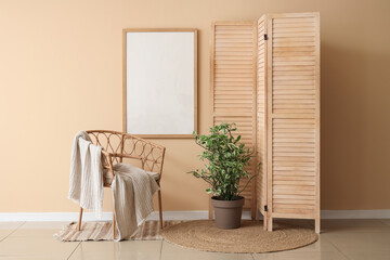 Wooden folding screen, wicker armchair and houseplant near beige wall in room