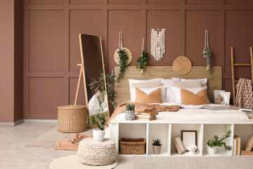 Comfortable bed, floor mirror and pouf near brown wall in interior of bedroom