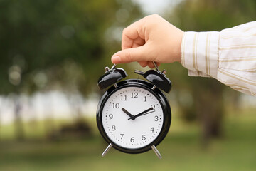 Female hand with black alarm clock in park, closeup