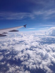 Obraz premium A vast expanse of cumulus clouds seen from an airplane window, with a vibrant blue sky and airplane wing in the foreground.