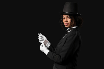 Young African-American magician with card in sleeve on black background