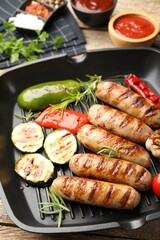 Pan with grilled sausages, vegetables, spices and sauces on table, closeup