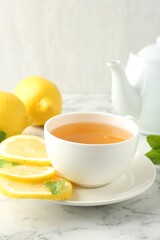 Aromatic tea in cup with lemons and mint on white marble table, closeup