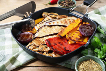 Tasty grilled vegetables and mushrooms in pan, spices and tongs on wooden table, closeup