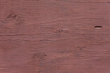 Close-up burnt red painted wooden surface with natural grain, knots, and aged texture, showcasing weathering due to exposure direct sunlight and aridity.