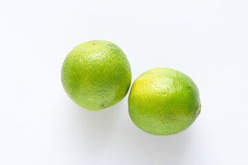 Two vibrant green limes are presented in a clean, minimalist closeup shot against a white background, highlighting their textured skin.