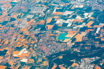 Aerial view of mixed terrain showing patchwork farmland, urban clusters, and a vivid turquoise reservoir. Winding river cuts through lush vegetation, highlighting diverse land use and natural features