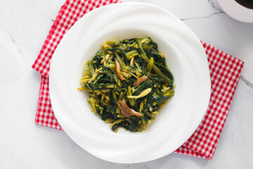 A plate of Manado-style stir-fried greens (Kangkung Bunga Pepaya) showcasing the fresh, leafy ingredients and aromatic spices.