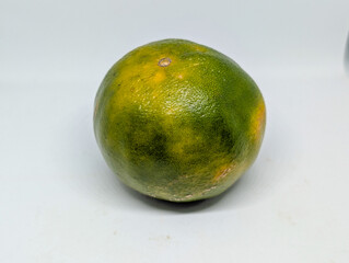 A single unripe orange with a green and yellow textured peel. Fresh organic citrus fruit, a source of vitamin C, isolated on a white background