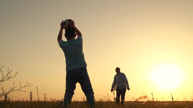 Happy family playing football. Dad kicks ball with his foot, child catches it. Family having fun playing football on lawn. Dad child play together, teamwork. Family sports football team play outdoor