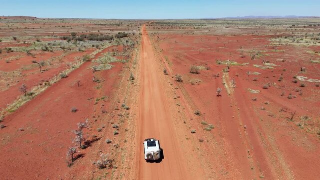 Aerial drone shot 4x4 offroad travel vehicle driving along a red dirt gravel road through the iconic desert of the outback at Karijini national park in the Pilbara, western Australia.