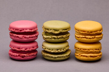 Three colorful macarons pink green yellow standing on gray
