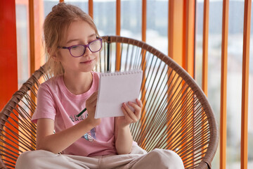 Girl with glasses writes in a notebook, focused and calm in soft daylight.
Young student enjoys creative learning and self-education at home.
Cozy study moment symbolizing imagination and mindfulness