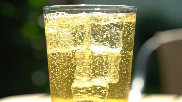 Refreshing close-up slow motion shot of ice cubes clinking in a tall glass filled with sparkling citrus beverage on a sunny outdoor table crisp, effervescent, mocktail