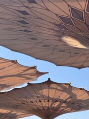 Intricate patterns of a large retractable umbrella seen from below against a clear blue sky at Prophet's Mosque, Medina.