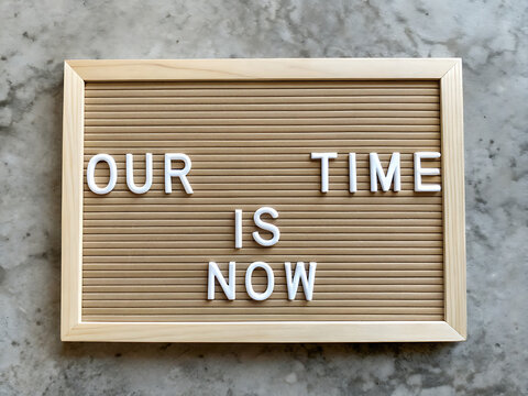 Inspirational message on a wooden letter board reading our time is now encouraging action and seizing opportunities in a modern setting