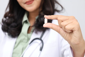 Close up photo of female doctor wearing doctor's coat holding medicine capsule with finger, isolated on white background.
