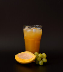 Tall glass of mango and green grape fruit juice with ice on black background.