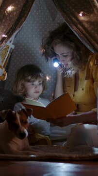 Loving mom reading book with little child in warm teepee tent surrounded by glowing lights vertical slow motion symbol of comfort security family connection and conscious parenthood