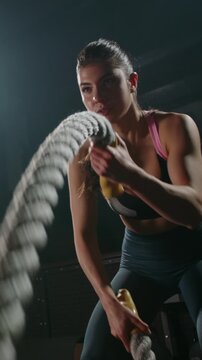 Fit woman in sportswear exercising with heavy battle ropes in dark gym slow motion strength training discipline power fitness motivation healthy lifestyle endurance concept vertical video