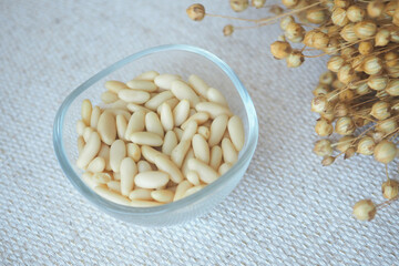 Pine nuts in a clear bowl with dried flowers nearby