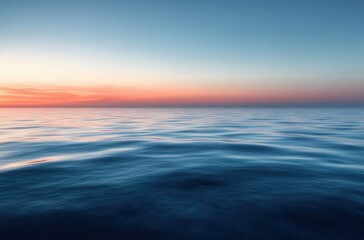 Obraz premium Calm ocean surface with gentle waves under a clear sky during a colorful sunset