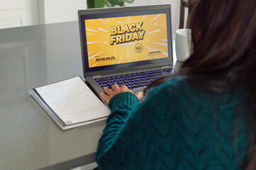 Woman searching online for Black Friday deals on her laptop. Young woman shopping online during Black Friday sale at home