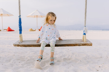 Little child girl on swings on tropical beach, enjoy childhood
