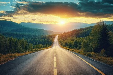 Fototapeta premium Empty paved road winding through a dense forested landscape with mountains in the background under a glowing sunset sky with dramatic clouds