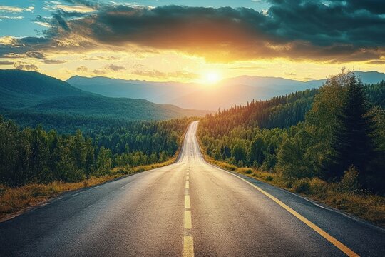 Empty paved road winding through a dense forested landscape with mountains in the background under a glowing sunset sky with dramatic clouds