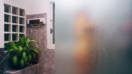 Female Silhouette Behind Steamed Glass While Showering in Tiled Bathroom with Plants, Side View Perspective, Intimate Wellness and Self Care Concept - Powered by Adobe