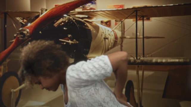 Woman with hand on lower back for backache beside a vintage biplane inside a museum building; discomfort.