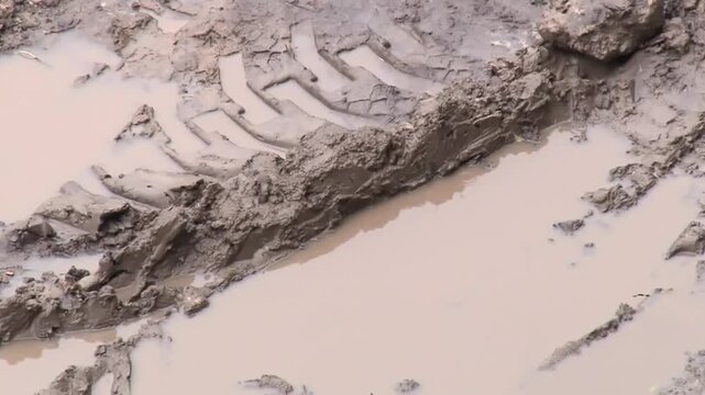 Dirt road with puddle and tire tread mark and raindrops falling on muddy road, mud on road in off-season