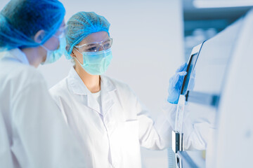 Two researchers in a GMP compliant cleanroom operate manufacturing equipment. They are following a Standard Operating Procedure for a Quality Assurance check on a product batch.