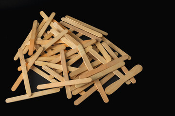 A scattered pile of wooden sticks of different sizes lies against a black background, creating a rustic texture. Concept of construction, nature, sustainability, DIY crafts, and raw materials.