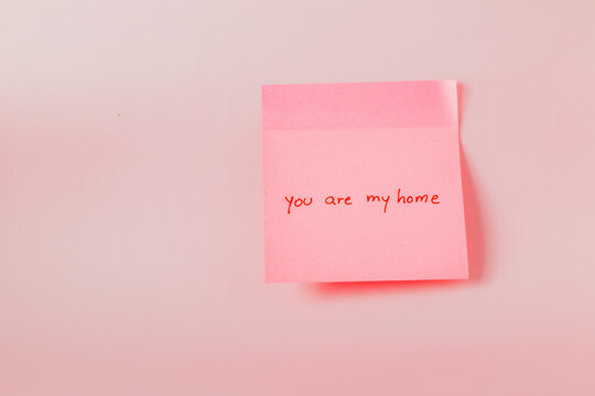 A pink sticky note with the words "You are my home" written on it. The note is placed on a pink background.
