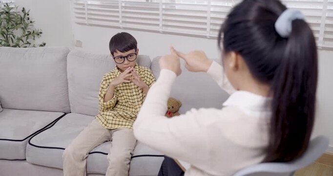 asian boy with adhd sitting on sofa during interactive therapy activity raising hands responding to female psychologist engaging in behavioral learning and communication techniques