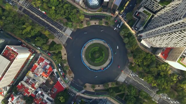 Overhead aerial spiral view of the Glorieta del Ahuehuete on Paseo de la Reforma in Mexico City, a symbolic roundabout in the Mexican capital, with low traffic on a weekday during daylight hours.