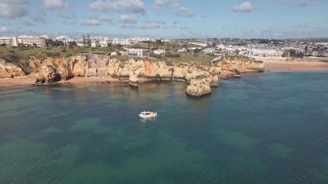 Aerial drone performs a helix orbit circling golden cliffs, rugged rock stacks, and turquoise water, revealing the pristine beaches and coastline near Lagos, Portugal.