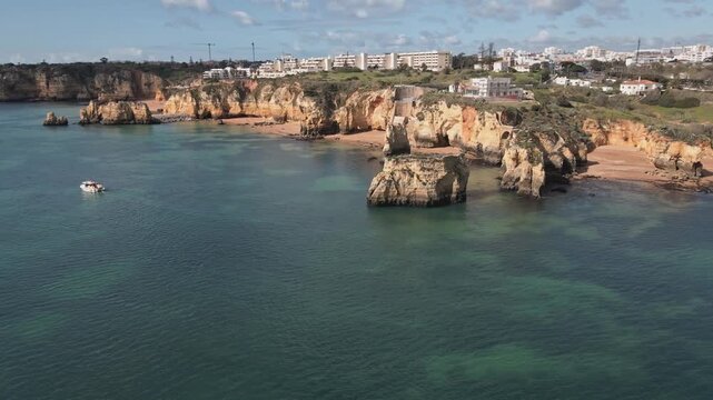 Aerial drone performs a helix orbit circling golden cliffs, rugged rock stacks, and turquoise water, revealing the pristine beaches and coastline near Lagos, Portugal.