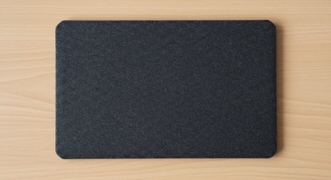 A dark grey felt mousepad with rounded corners placed on a wooden desk surface for commercial usage and mockups
